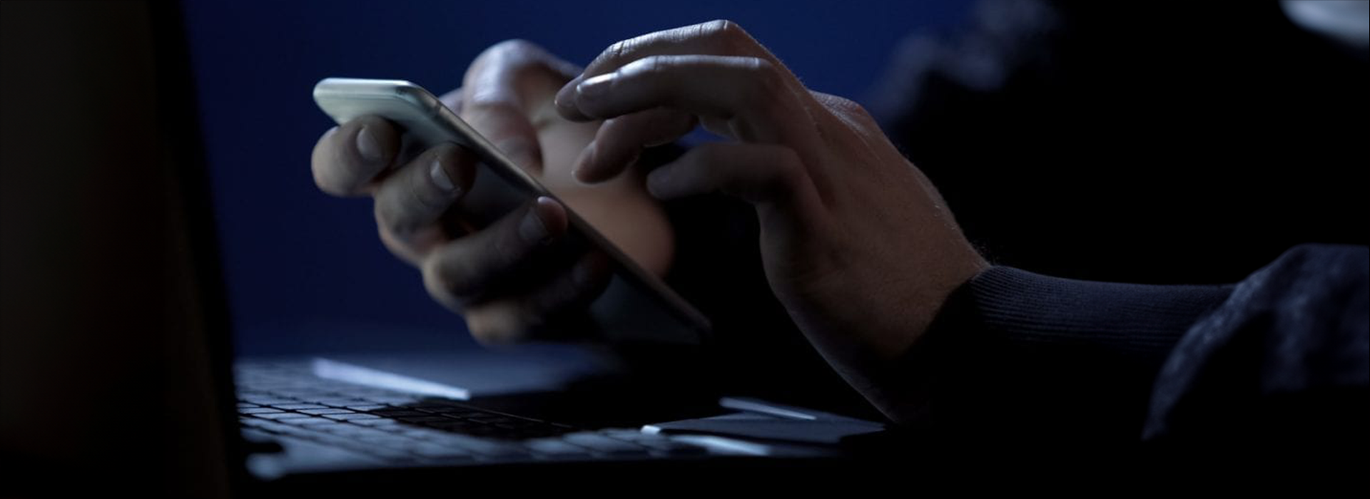 hands on a mobile phone in front of a laptop