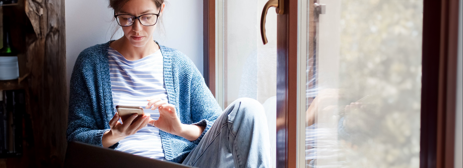 woman sitting in a window looking at her phone